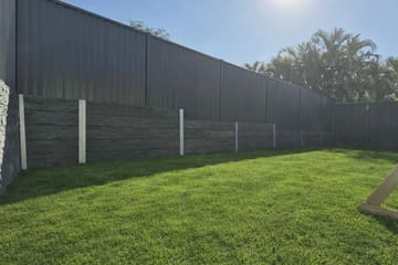 Tiered Blakeview stacked-stone concrete sleeper retaining walls below a Woodland Grey Colorbond fence