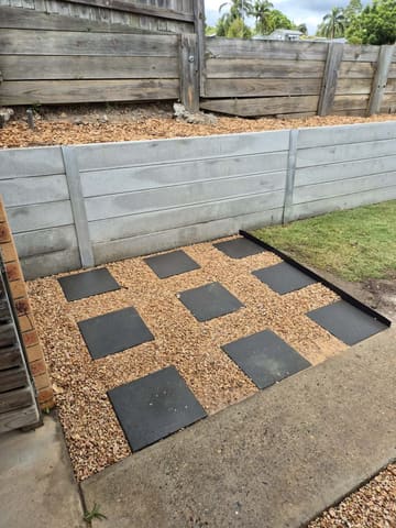 Charcoal pavers set in gravel in front of a concrete sleeper retaining wall