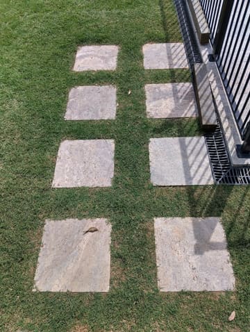 Travertine stepping stones set into new turf beside a black fence