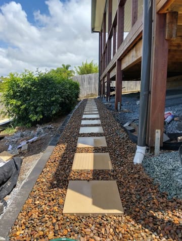 Stepping-stone pavers in pebbles along a side path under a deck