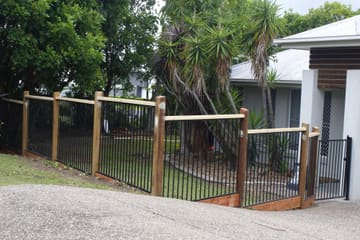Front fence with timber posts and black aluminium panels stepping down a sloping driveway