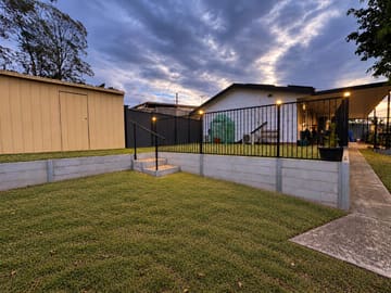 Concrete sleeper retaining walls with built-in steps, new turf and a black fence at dusk
